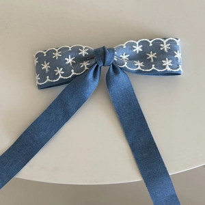 Detail van denimblauwe haarstrik met wit kant borduursel en lange hangende linten