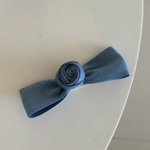 Detailopname van een blauwe denim haarstrik met een stoffen roos op een witte tafel