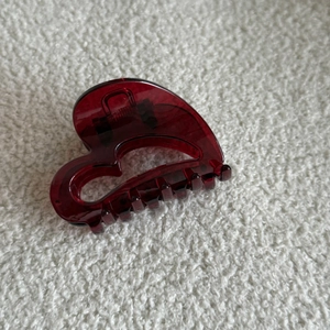 Detailed close-up of translucent burgundy heart-shaped hair claw clip on soft white fabric