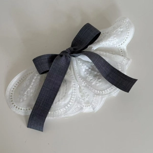 Detail of elegant white lace hair clip with dark grey bow and intricate embroidery