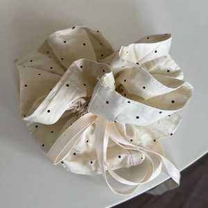 Detail of a soft cream polka dot fabric storage bag with a satin drawstring ribbon