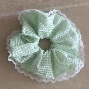 Détail d'un chouchou à carreaux vert clair avec bordure en dentelle blanche sur pierre