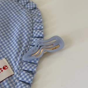 Detail der hellblauen gewellten Acryl-Haarklammer auf blau kariertem Stoff mit Metallbasis