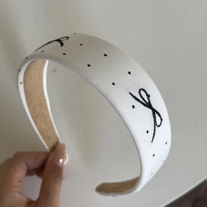 Detailed shot of a white polka dot fabric headband with embroidered black bows and lining