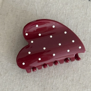 Close-up of a glossy deep red hair claw clip with white polka dots and heart-shaped design