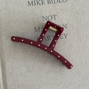 Close-up of a burgundy claw clip with white polka dots and a golden metal spring
