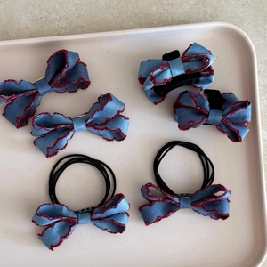 Detail of blue denim bow hair clips and ties with red wavy scalloped edge embroidery