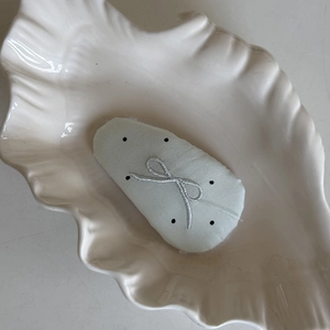 Close-up of green polka dot fabric hair clip with embroidered bow on seashell plate