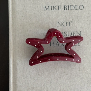 Detail view of a star-shaped burgundy hair claw clip with white polka dots on a book cover
