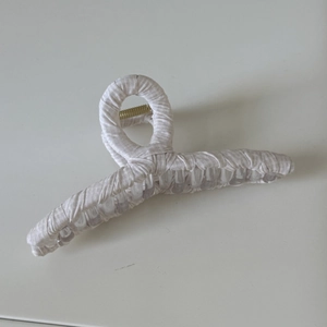 Détail d'une pince à cheveux enveloppée de tissu blanc texturé avec ressort doré