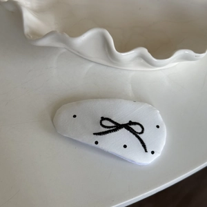 Detailed view of white fabric hair clip with black embroidered bow and polka dots