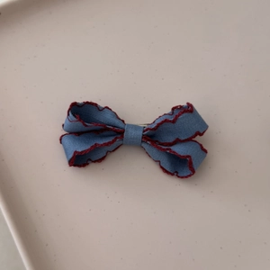 Detail of denim bow hair clip with red scalloped edges and textured fabric finish