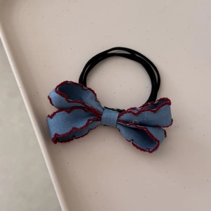 Detail of blue denim bow hair tie with red scalloped edges and black elastic band
