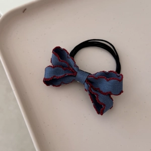 Close-up of denim bow hair tie with red scalloped embroidery edge and black elastic