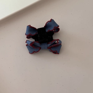 Detail of a dark blue fabric bow hair clip with decorative red scalloped edge stitching