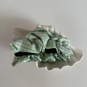 Close-up of a large blue and yellow plaid fabric hair claw clip on a white shell tray