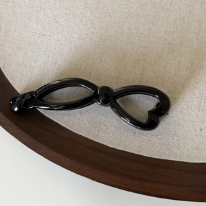 Détail d'une pince banane noire brillante en forme de nœud avec découpe en forme de cœur