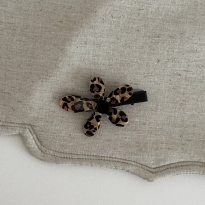 Detail view of French leopard print flower hair clip on a textured linen background