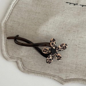 Close-up of leopard print flower hair clip on a textured beige fabric background