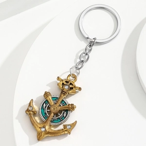 Vintage gold anchor and helm keychain with crystal accents on a white geometric stand