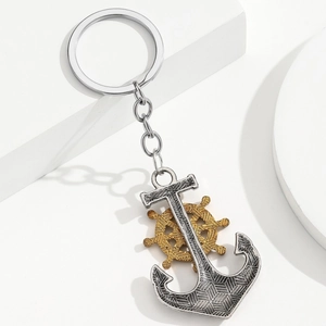 Detail of silver nautical anchor and gold ship wheel keychain on a white stone background