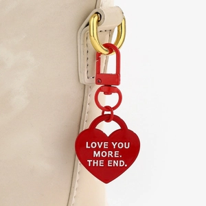 Dettaglio di un ciondolo a cuore rosso con stampa Love You More attaccato a borsa