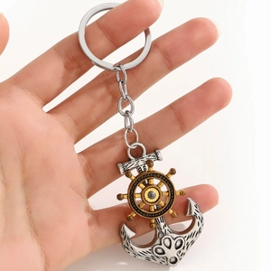 Detail of silver anchor and golden ship wheel keychain held in hand on white background