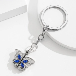 Porte-clés papillon argenté avec strass bleus posé sur des blocs blancs épurés