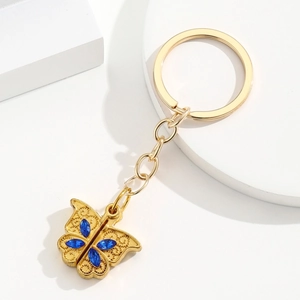 Porte-clés papillon doré avec cristaux bleus et détails filigranes sur fond blanc