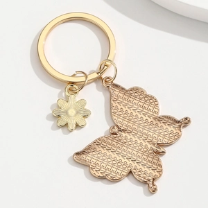 Porte-clés papillon doré et breloque marguerite avec textures gravées sur fond blanc