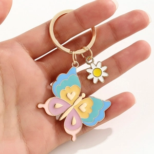 Détail d'un porte-clés papillon en émail avec marguerite tenu dans la main d'une femme