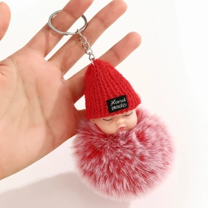 Détail d'un porte-clés poupée endormie avec pompon rose et bonnet en tricot rouge