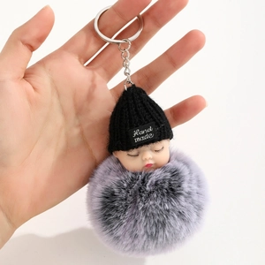 Détail d'un porte-clés poupée bébé endormie avec un pompon moelleux en fausse fourrure