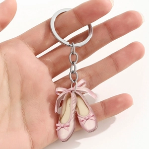 Detail of pink satin ballet slippers keychain with silk ribbons held against white background