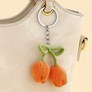 Close-up of orange knitted tulip keychain with green bow on a white leather bag