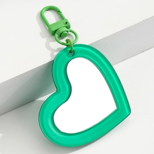 Detail shot of a bright green heart-shaped mirror keychain on a white geometric stand