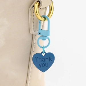 Gros plan du porte-clés coeur bleu avec gravure Thank You attaché à un sac en cuir beige