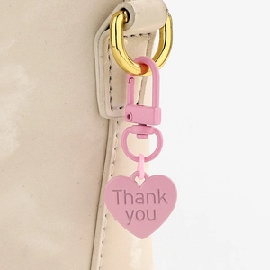 Gros plan du porte-clés cœur rose avec gravure Thank You sur un sac en cuir blanc