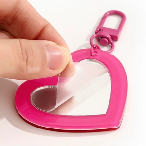 Close-up of pink heart-shaped mirror keychain with protective film being removed