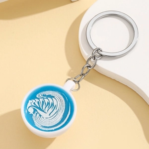 Detail of miniature coffee cup keychain with blue latte art on a minimalist background