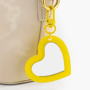 Detail of yellow heart-shaped mirror pendant with rotating metal clasp on beige leather bag
