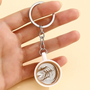 Detail of creative mini coffee cup keychain with latte art heart pattern held in hand