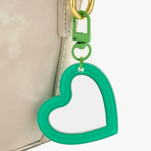 Detail of a bright green heart-shaped keychain accessory on an off-white glossy handbag