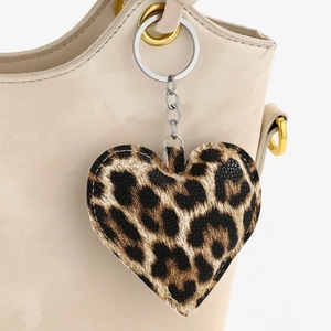 Close-up of heart-shaped leopard print leather keychain hanging on a beige handbag