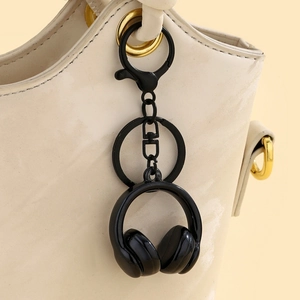Close-up of a matte black headphone-shaped keychain attached to a cream-colored bag