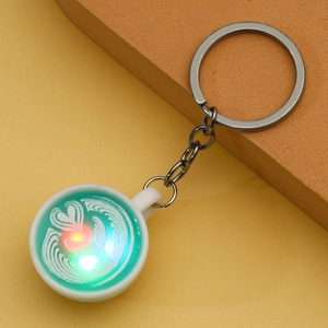 Close-up of a glowing coffee cup keychain with green latte art and metal ring