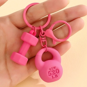 Pink fitness keychain with dumbbell and kettlebell charms held to show scale and detail