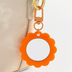 Macro shot of an orange flower keychain mirror attached to a beige leather handbag strap