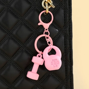 Macro shot of pink kettlebell and dumbbell keychain on a black quilted bag strap