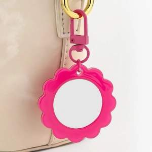 Detail of rose pink flower mirror charm hanging on a beige bag with golden clasp